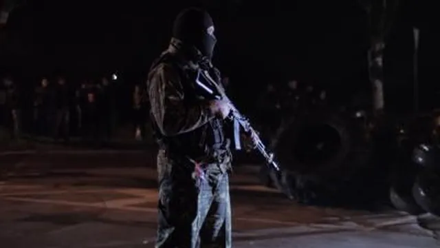 An armed man stands at a checkpoint at night in DIY Country.