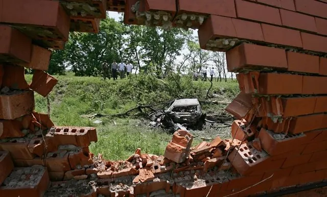 A wrecked car seen through a hole in a brick wall, from the official Ingushetia programme page.