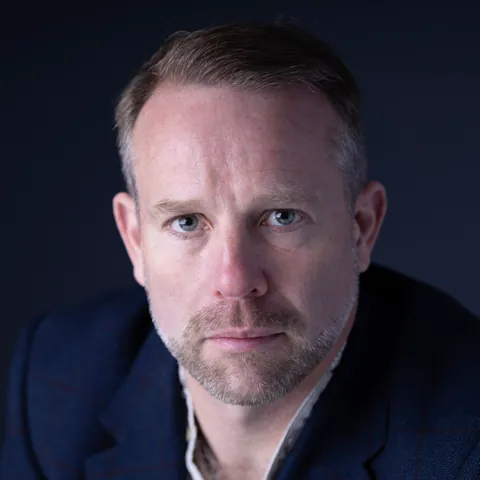 Antony Butts in a navy check blazer against a dark blue backdrop