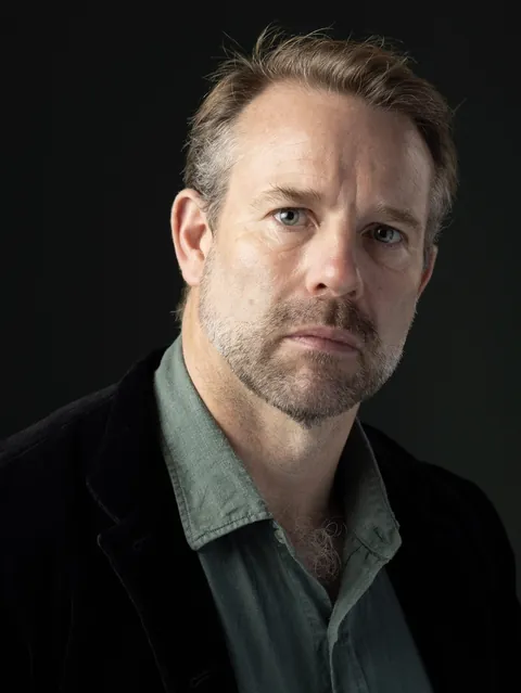 Antony Butts in a green shirt and black jacket against a dark background