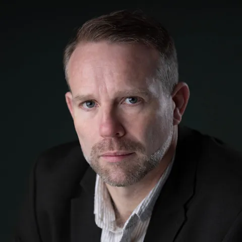 Antony Butts in a dark jacket against a near-black backdrop